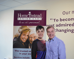 Couple smiling in front of Home Instead poster